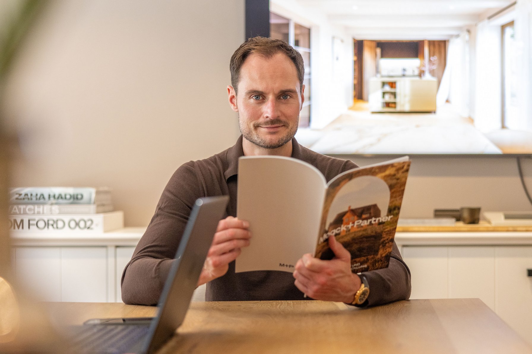 Geschäftsführer Maximilian Mogck sitzt an einem Tisch und hält eine Broschüre in den Händen