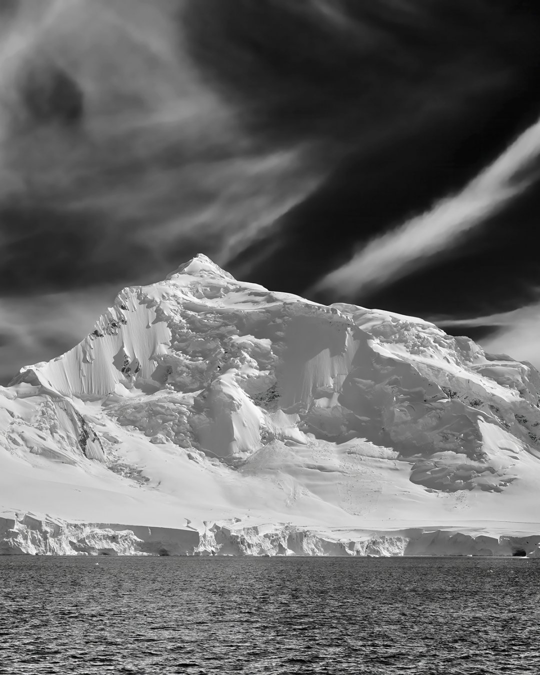 Schwarz-Weiß Fotografie von schneebedecktem Berg am Meer mit Schleierwolken