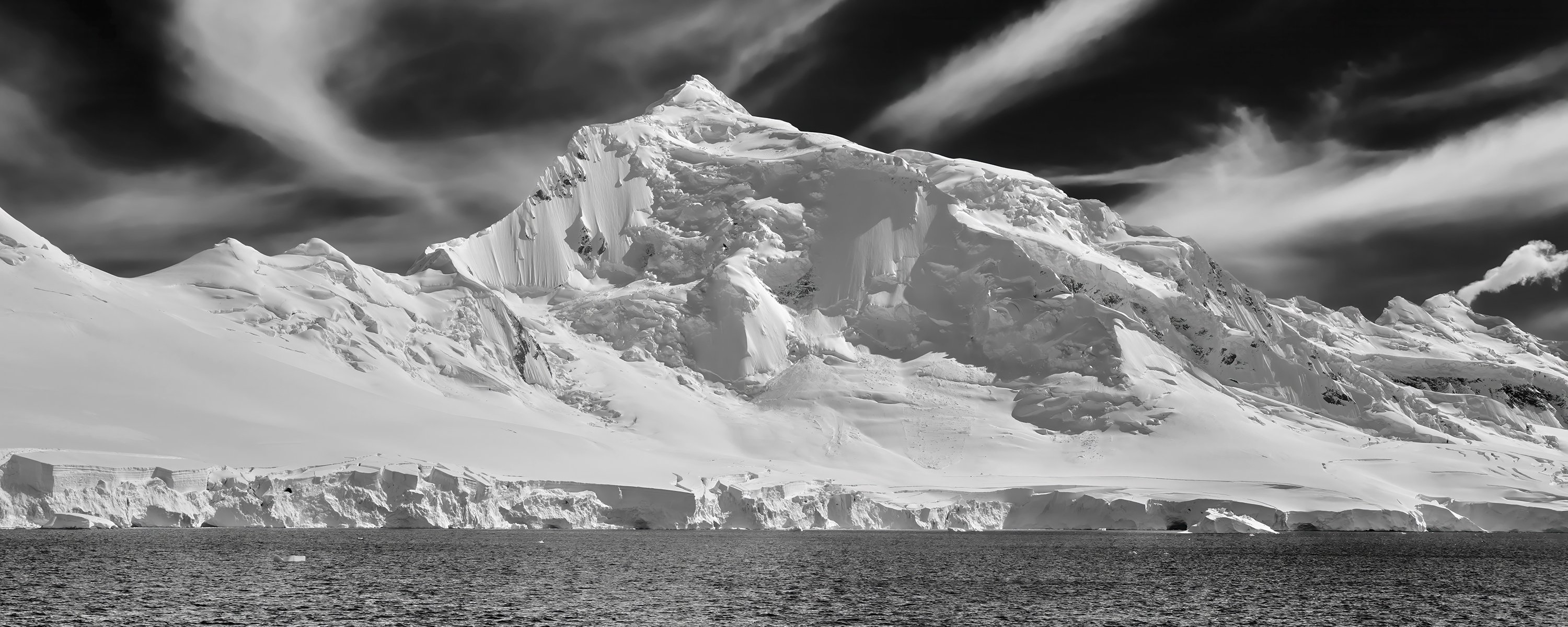 Schwarz-Weiß Fotografie von schneebedecktem Berg am Meer mit Schleierwolken